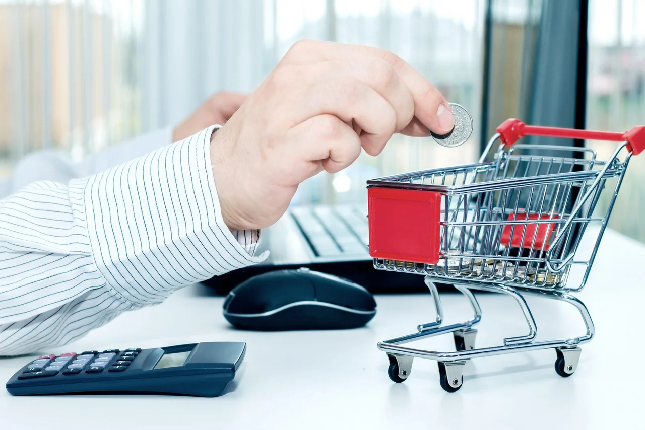 A hand placing a coin in a miniature shopping cart